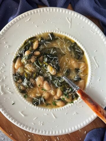 An overhead photo of white beans and spinach soup on a white bowl with a tablespoon.