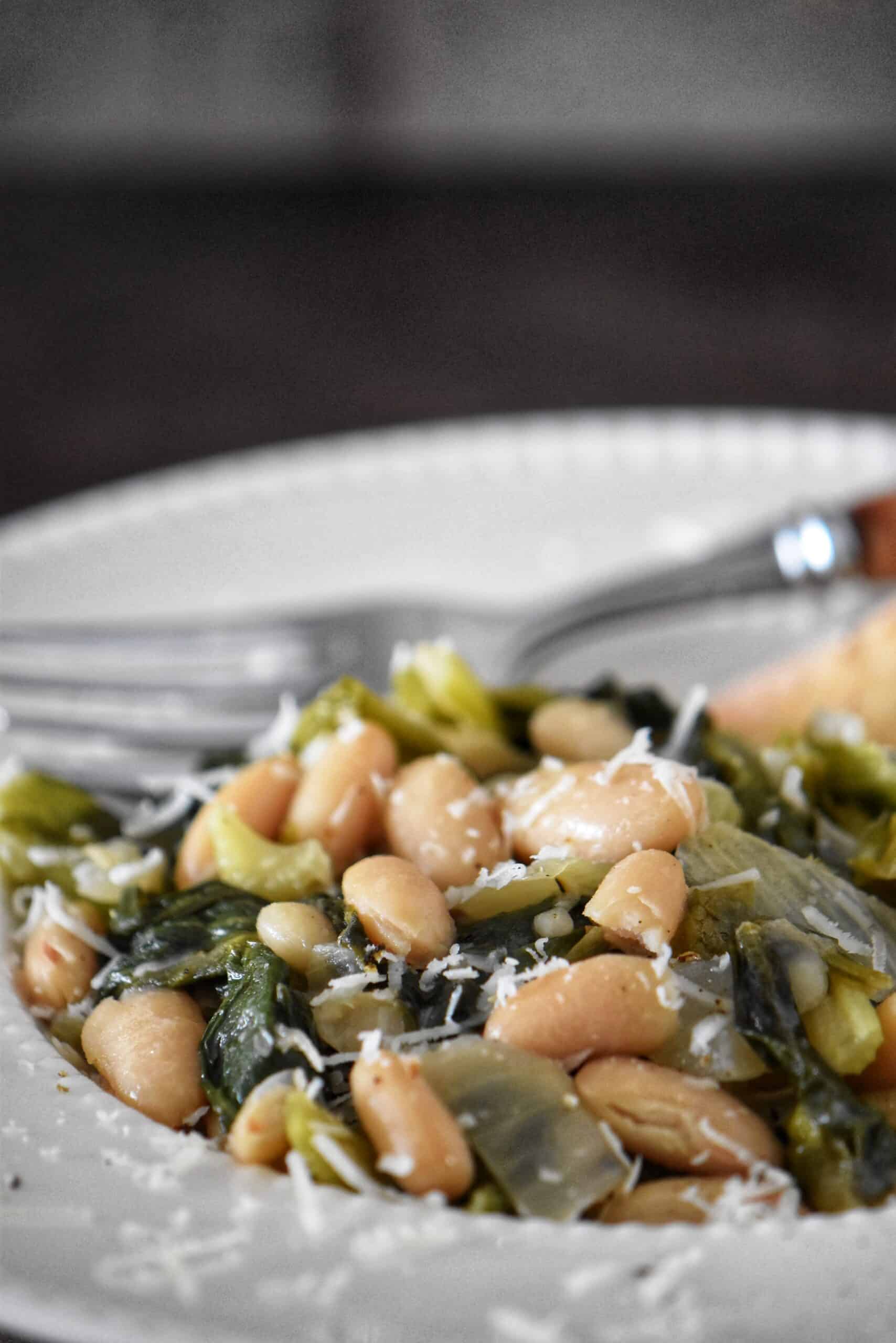 A close-up photo of beans and greens (Italian escarole) in a bowl.