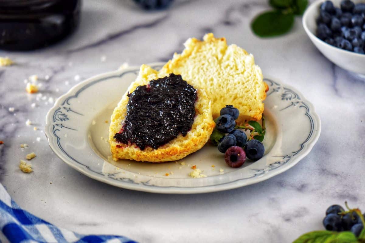 Blueberry jam in a mason jar surrounded by fresh berries.