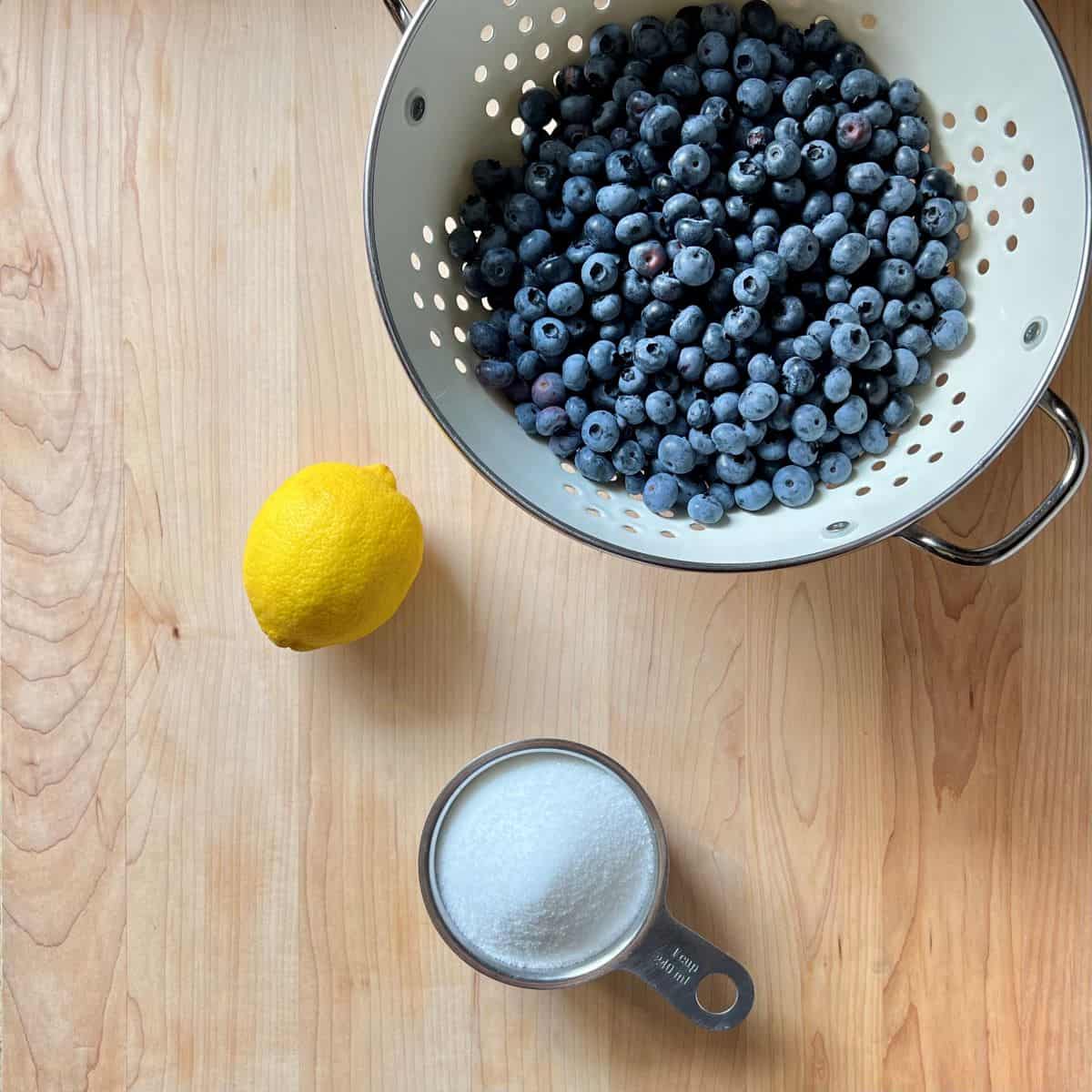 The ingredients to make blueberry jam on a wooden board.