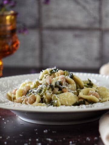 An Italian pasta dish with white beans and escarole on a white plate.