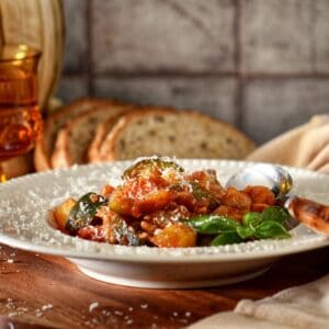 White shallow bowl filled with ciambotta, served with fresh bread.