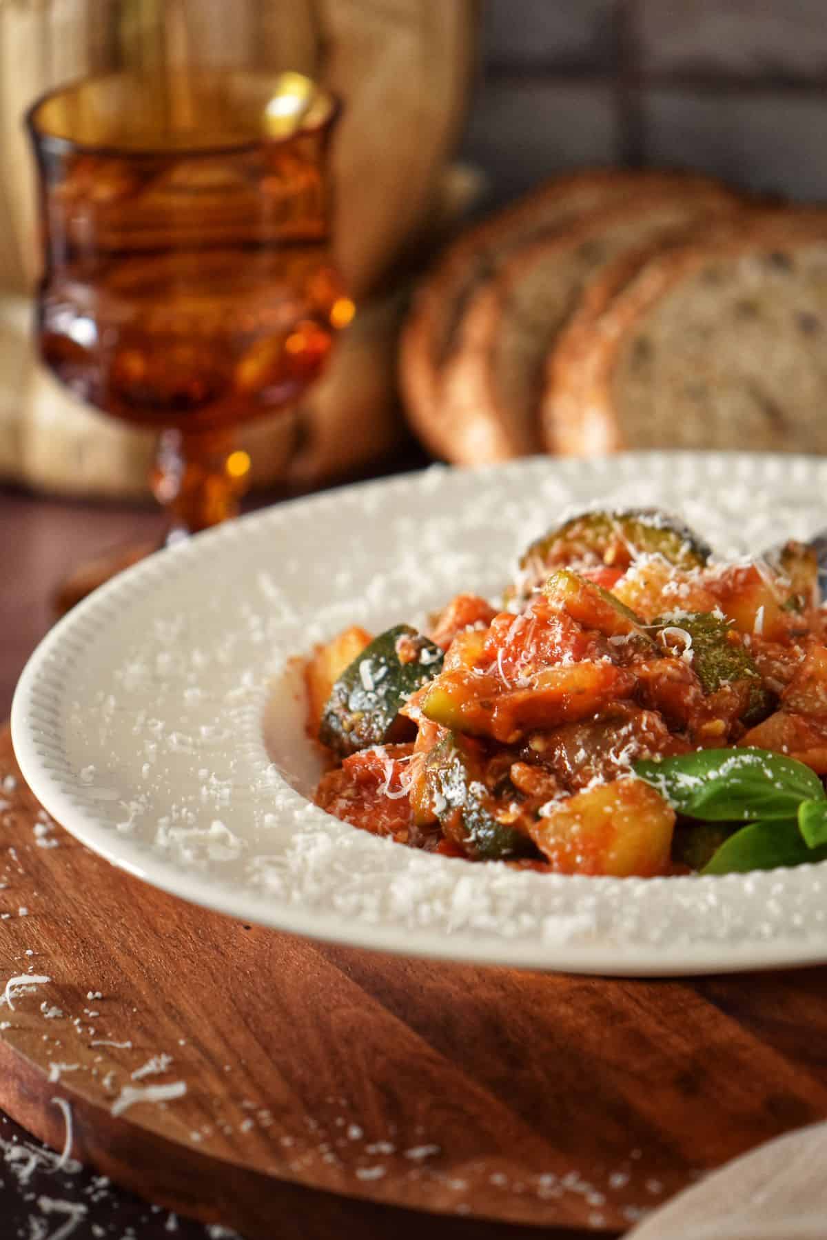 White shallow bowl filled with homemade Italian vegetable stew served with fresh bread.