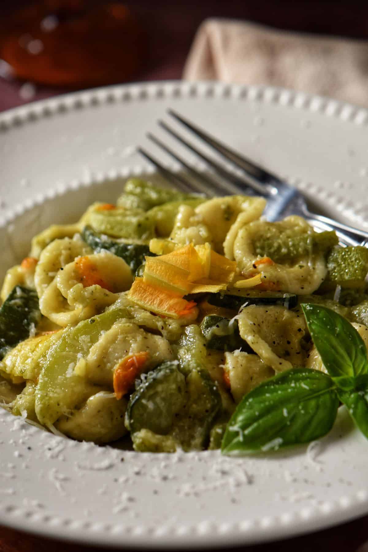 Zucchini pasta on a white bowl garnished with fresh basil and zucchini flowers.