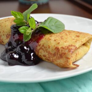 Cheese blintz garnished with blueberry sauce and mint leaves.