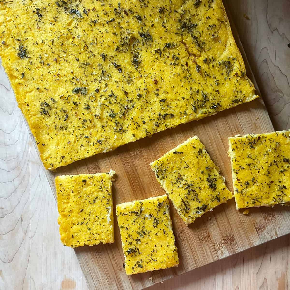 A few pieces of polenta pizza with herbs on a wooden board.