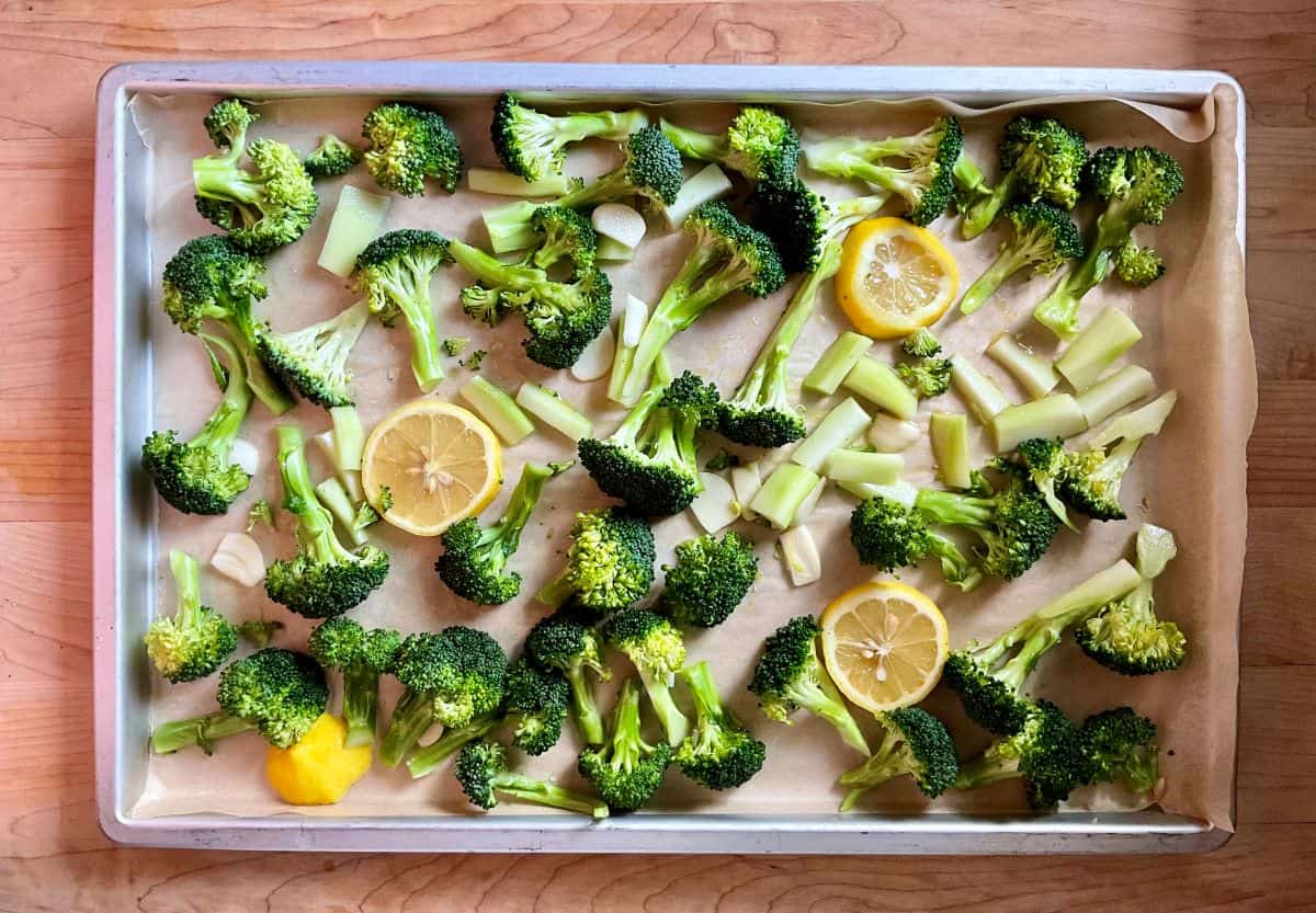 Raw broccoli and lemon slices on a parchment lined sheet pan.
