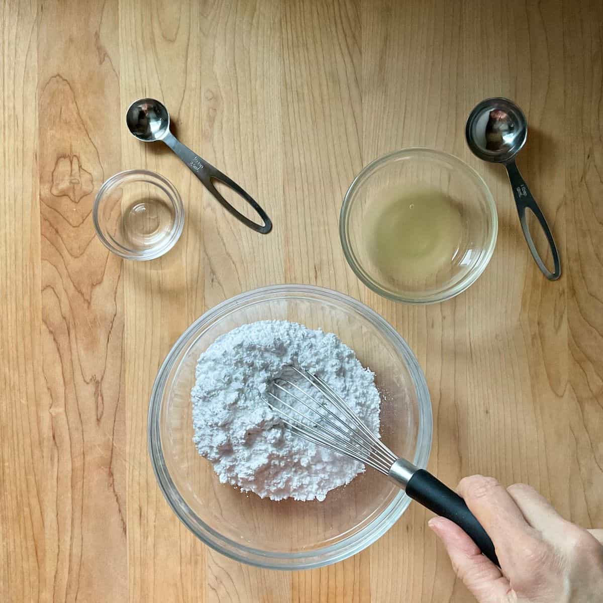 Lemon juice being whisked into icing sugar to make lemon icing.