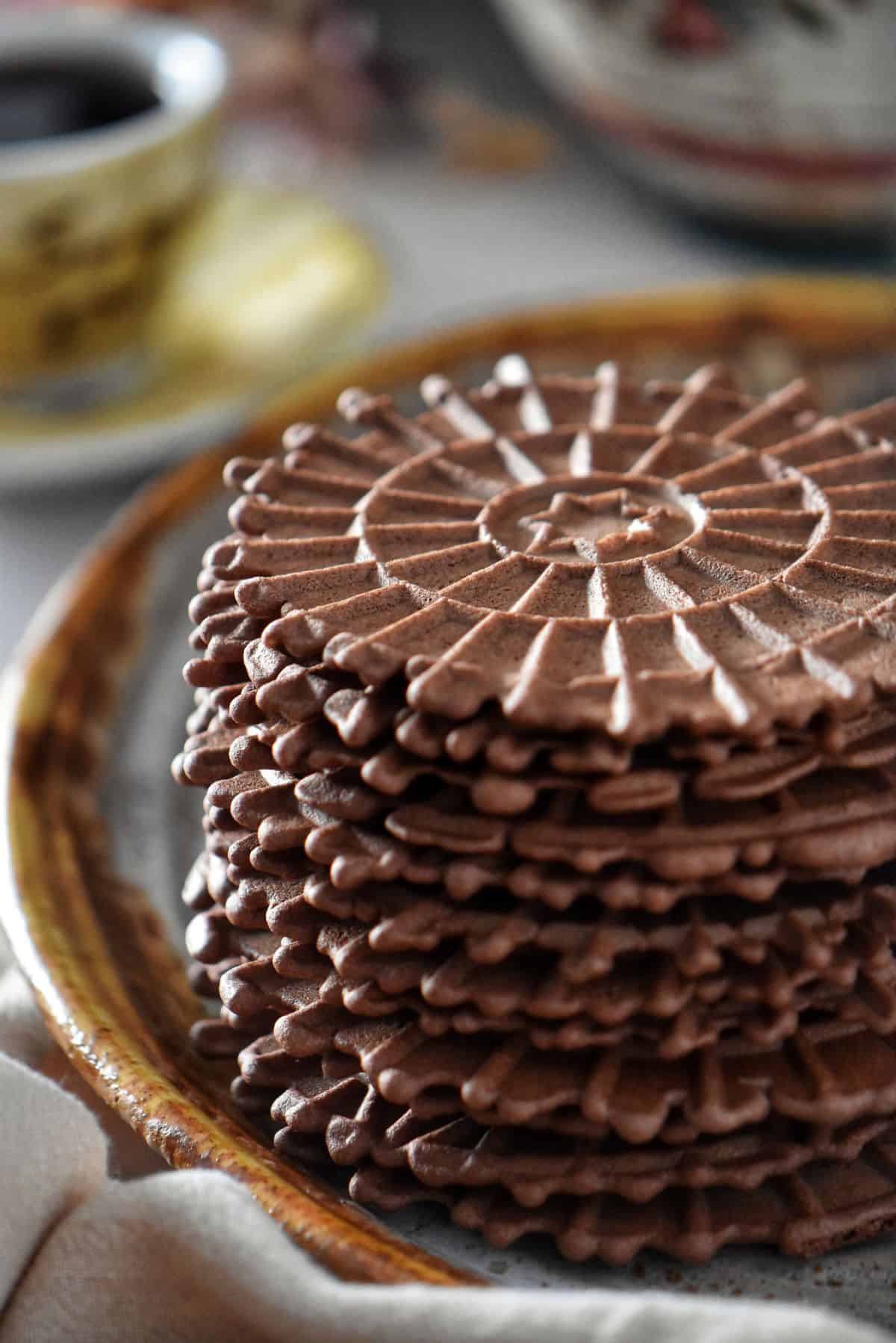 A stack of chocolate pizzelle on a platter.