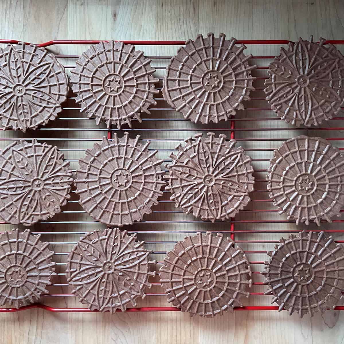 Chocolate pizzelle on a wire rack.