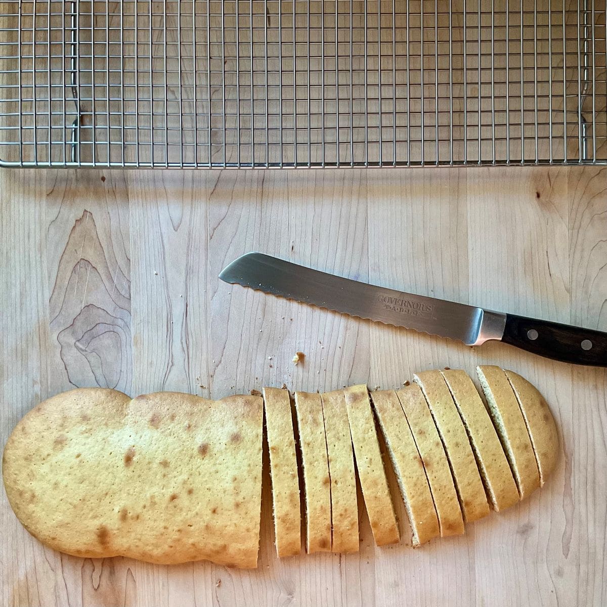Sliced Italian cookies on a wooden board next to a cooling rack.