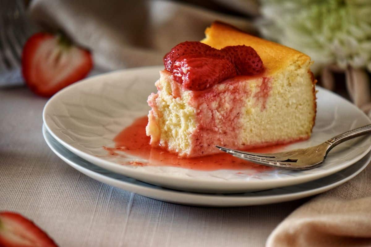 A slice of ricotta cheesecake garnished with roasted strawberries on a white plate.