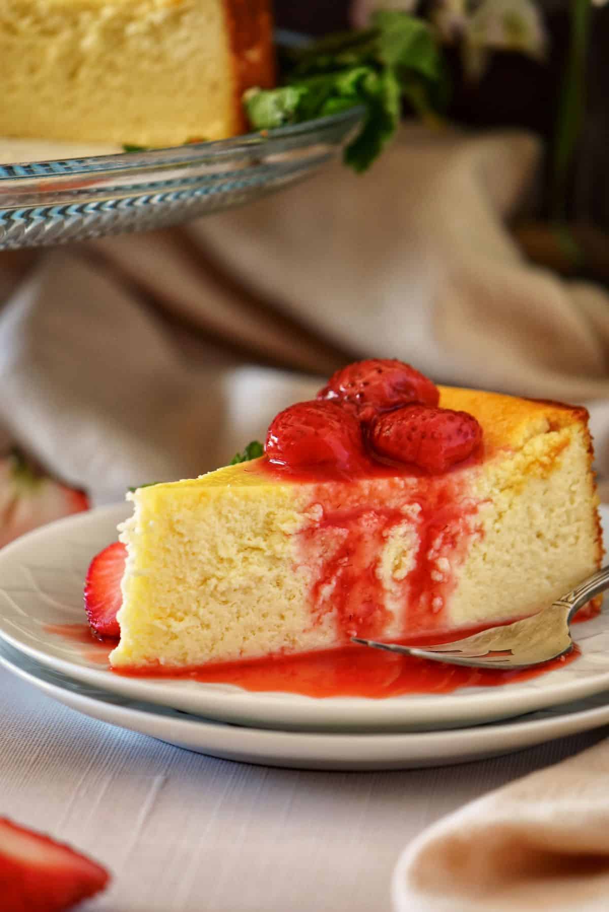 A slice of ricotta cheesecake garnished with roasted strawberries on a white plate.