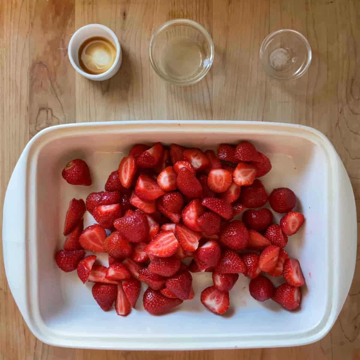 Hulled and halved strawberries in a white baking dish.