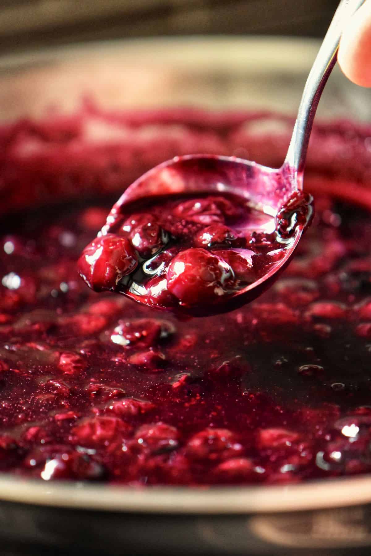 Ladle lifting homemade berry compote from a pan.