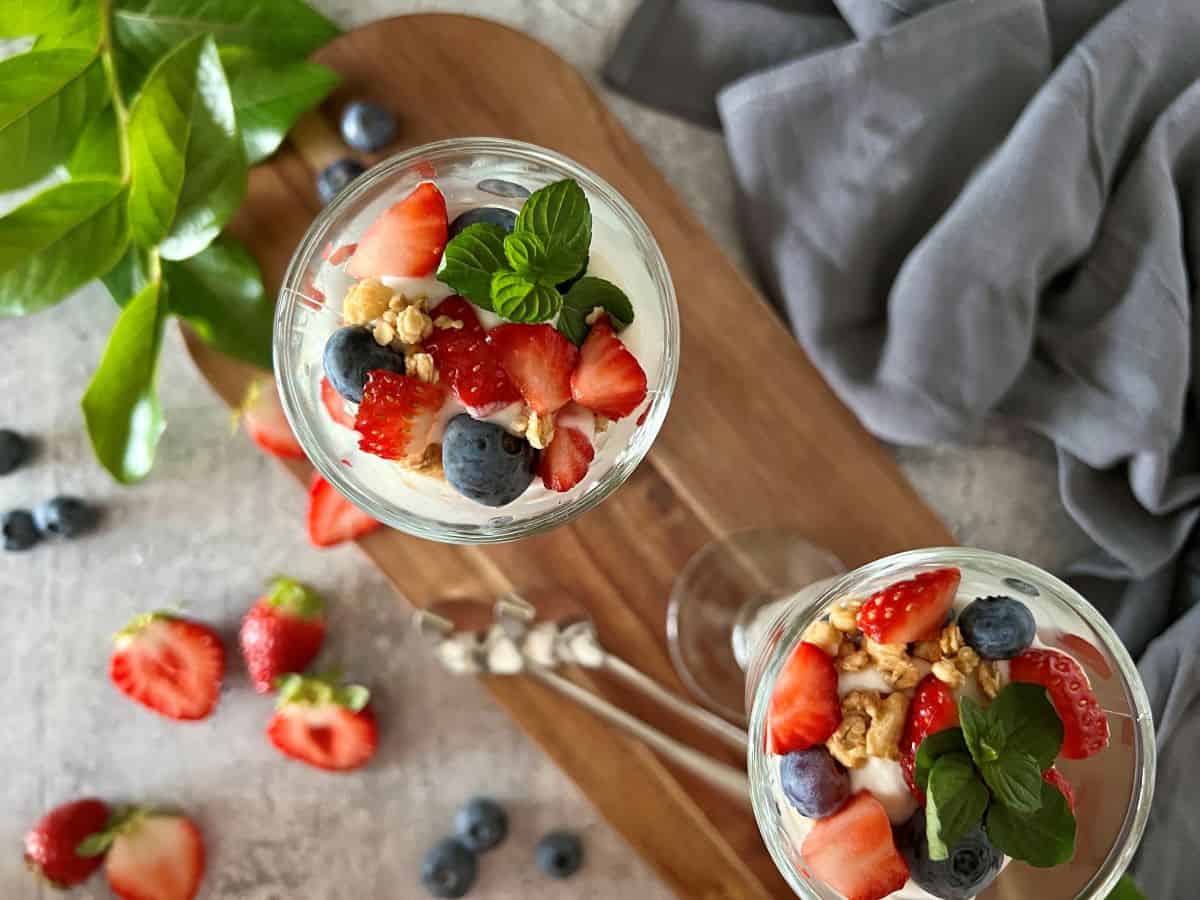 Top view of a parfait glass filled with layers of whipped ricotta cheese, fresh strawberries, blueberries, and crunchy granola, beautifully arranged and topped with a sprig of mint.