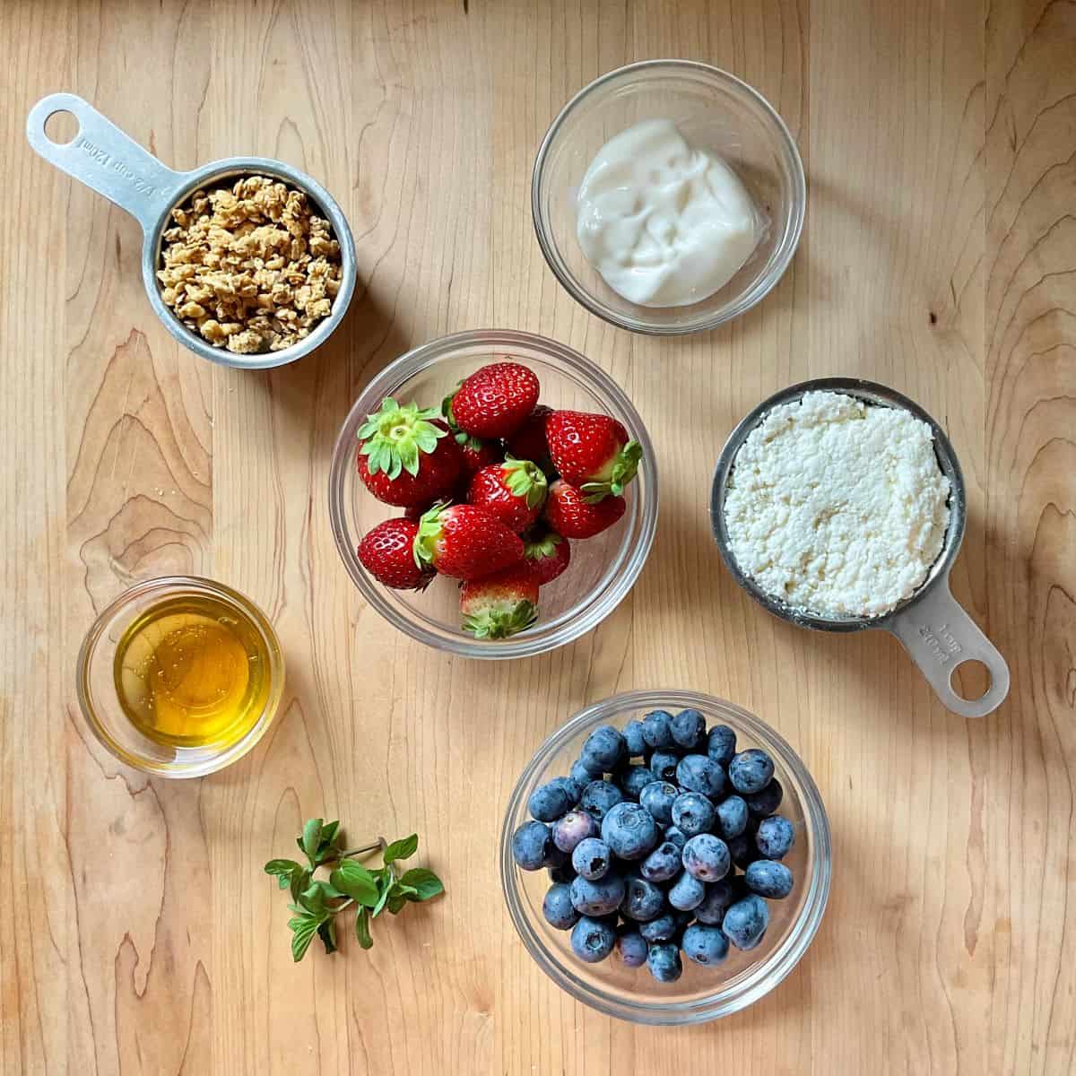 Ingredients to make a fruit parfait in bowls and measuring cups.