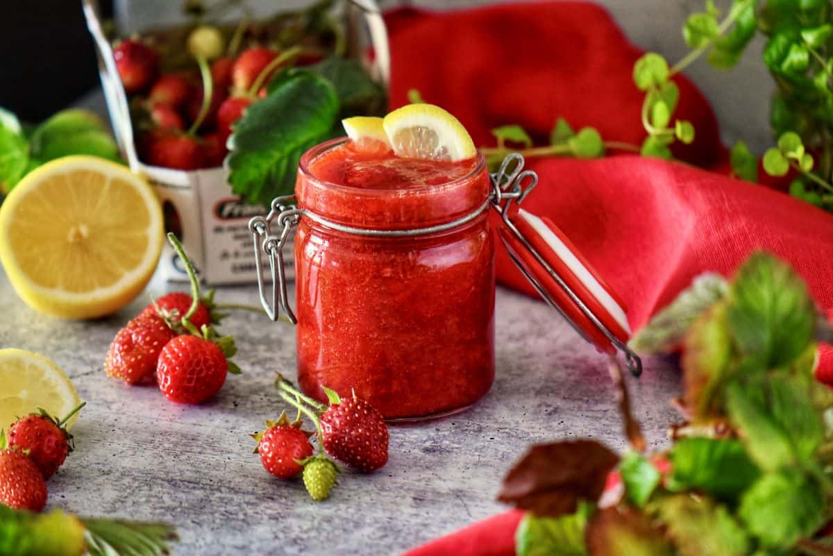 A Mason jar of strawberry sauce next to fresh strawberries.