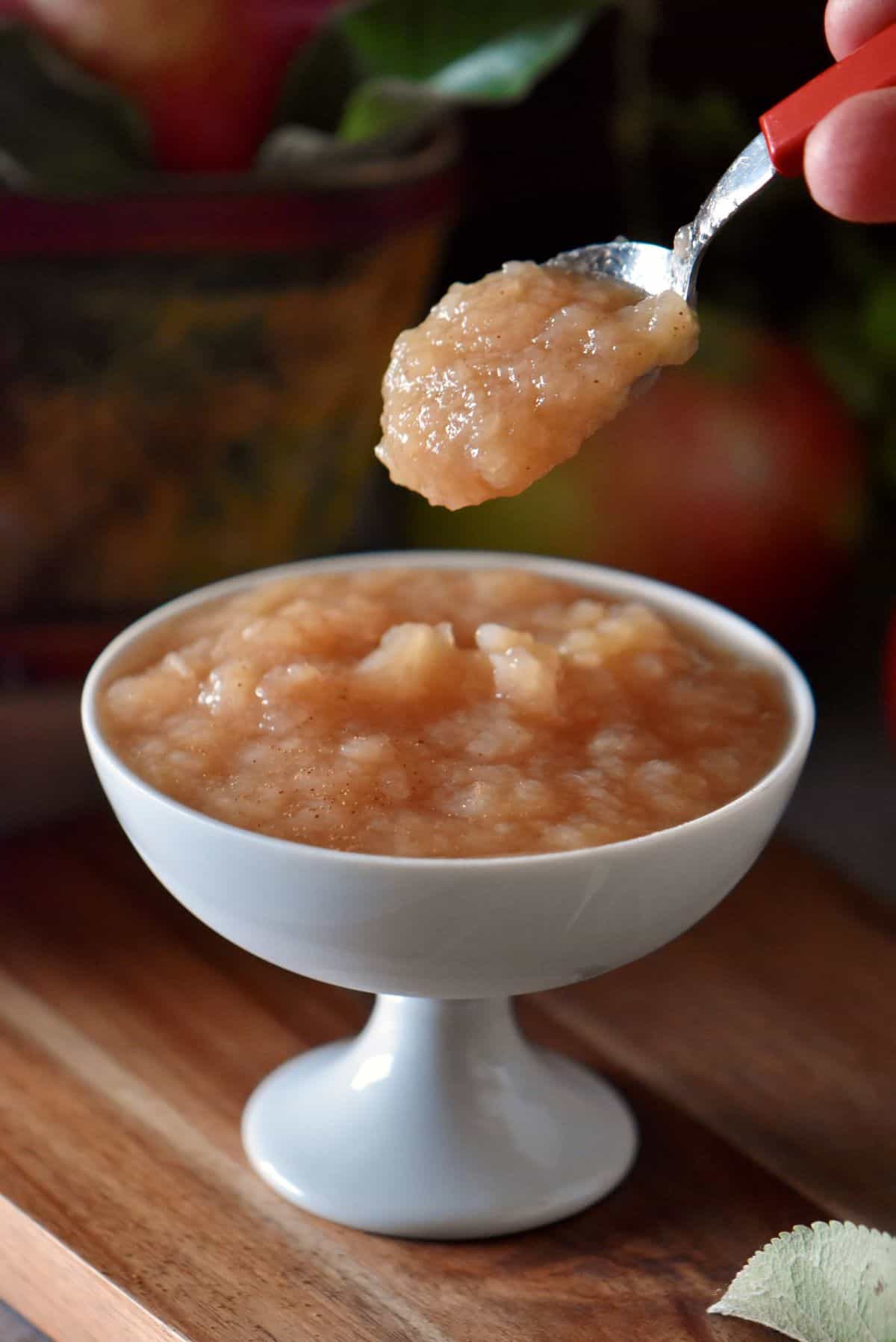 A spoonful of homemade applesauce being held over a white dessert bowl of applesauce.