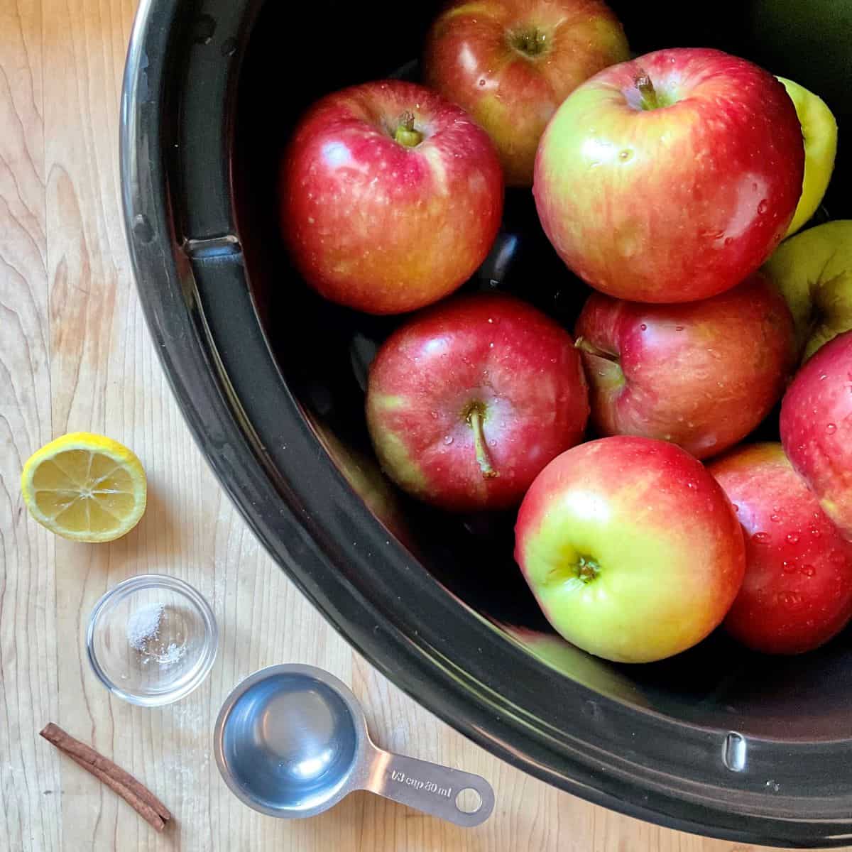 Ingredients for slow cooker applesauce on a wooden surface including red apples in a crockpot.