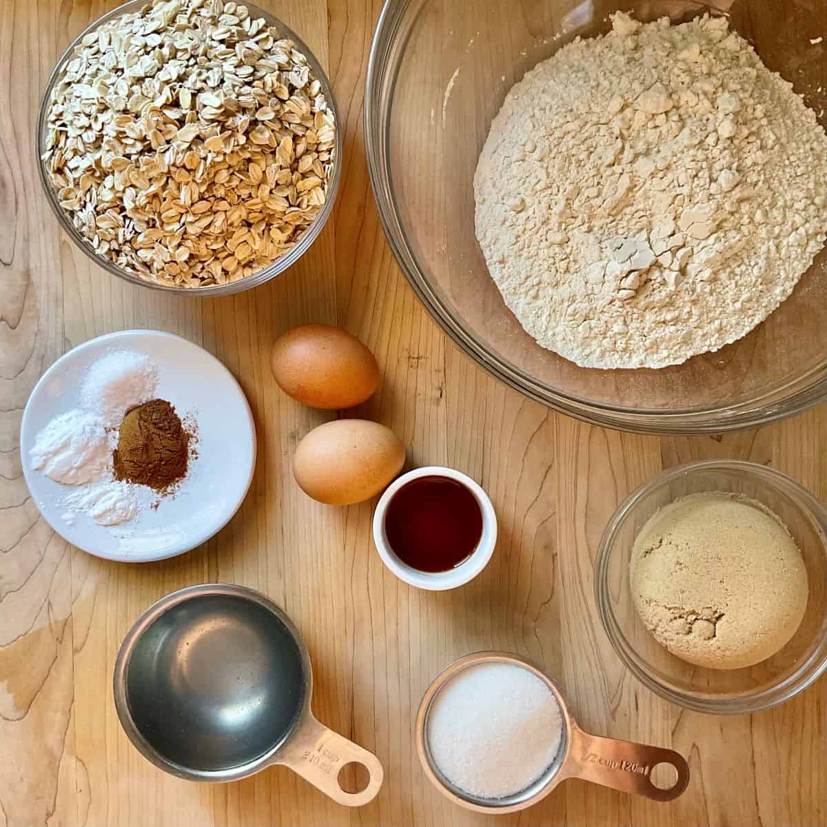 Ingredients for dairy-free oatmeal cookies, including coconut oil, oats, flour, sugar, brown sugar, eggs, and vanilla extract, neatly arranged on a kitchen counter.