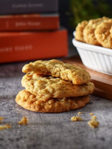 Small stack of coconut oatmeal cookies with a bite taken from the top cookie, revealing the chewy texture inside.