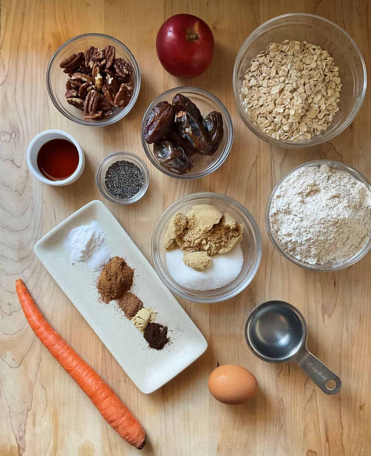 Ingredients to make carrot cookies, including oats, flour, sugar, brown sugar, carrot, pecans dates and spices neatly arranged on a kitchen counter.