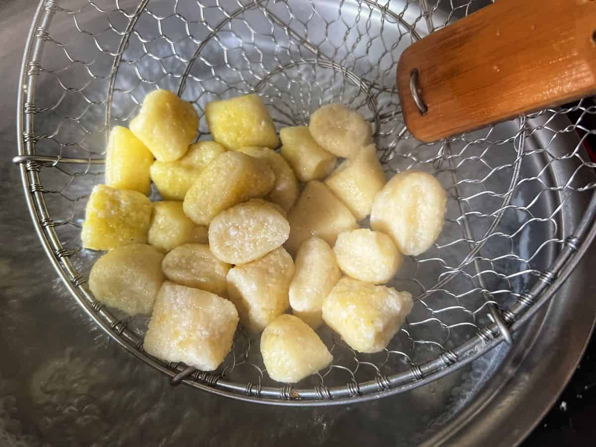 Gnocchi in a spider strainer over a pot of boiling water.