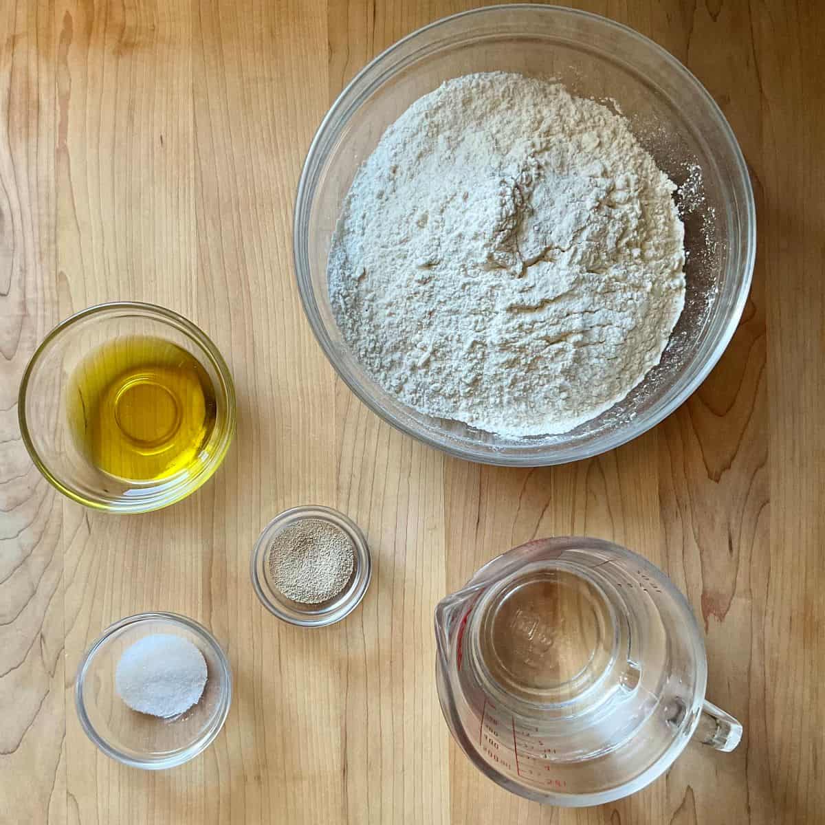 Flour, yeast, olive oil, salt and water measured for bread baking.
