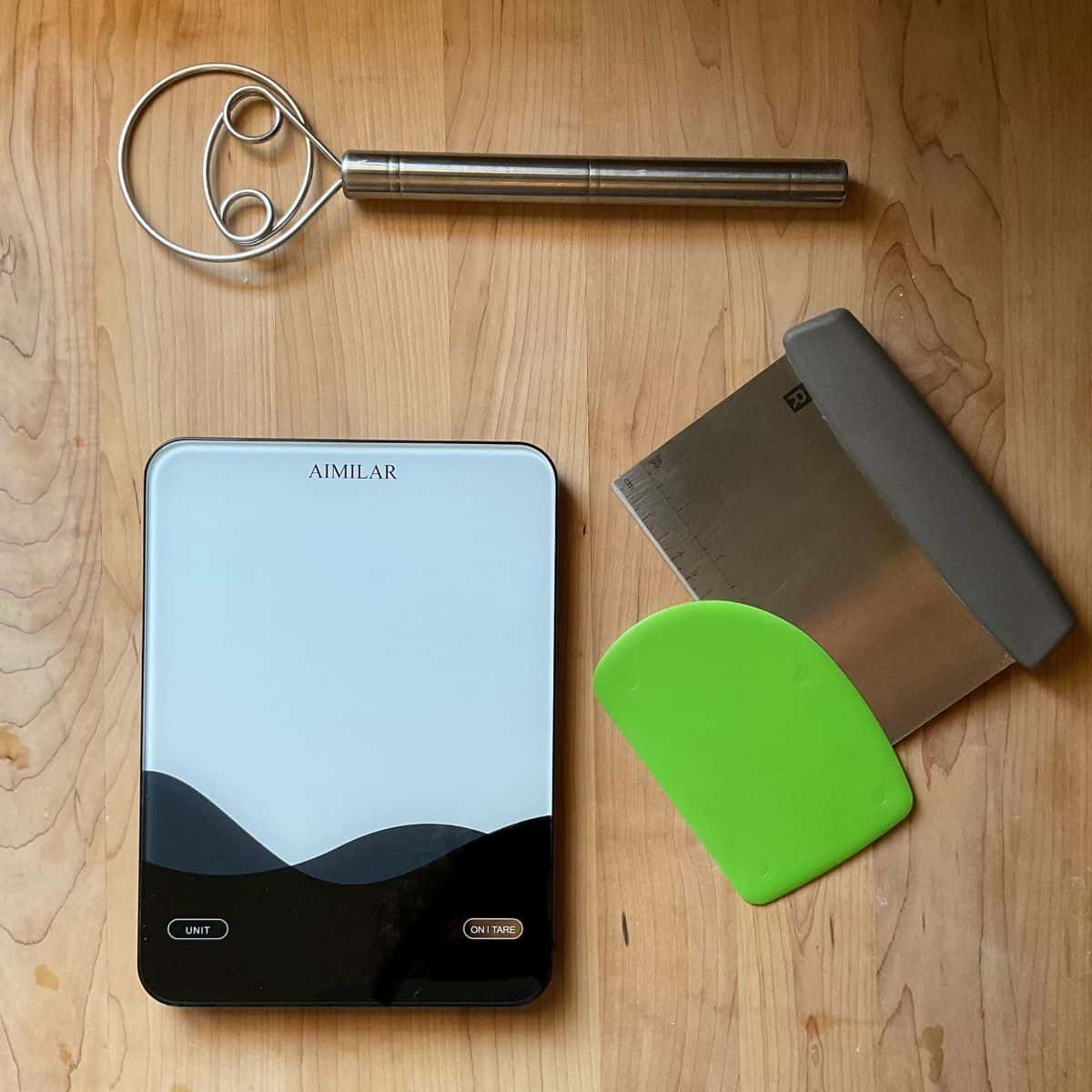 Baking tools for making homemade Italian panini bread including a scale and bench scraper.