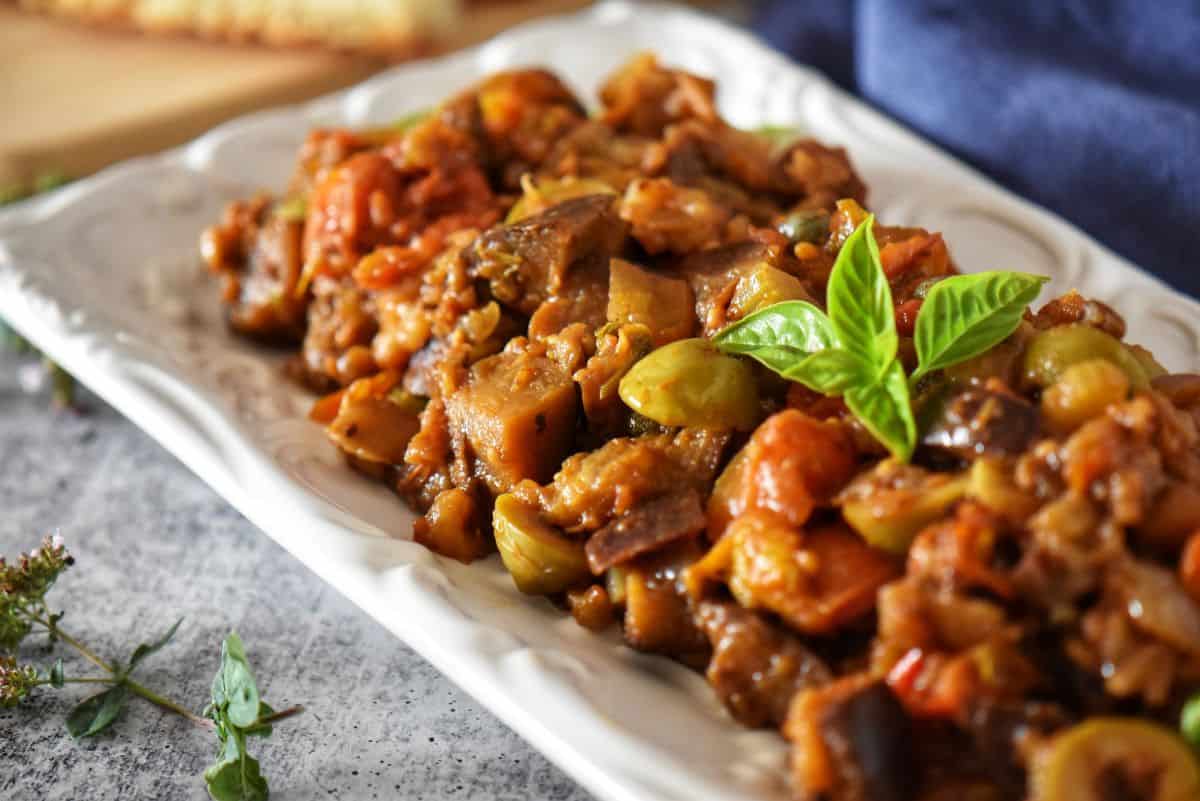 Healthy Mediterranean eggplant caponata served close-up, highlighting textures of eggplant, tomatoes, and olives.