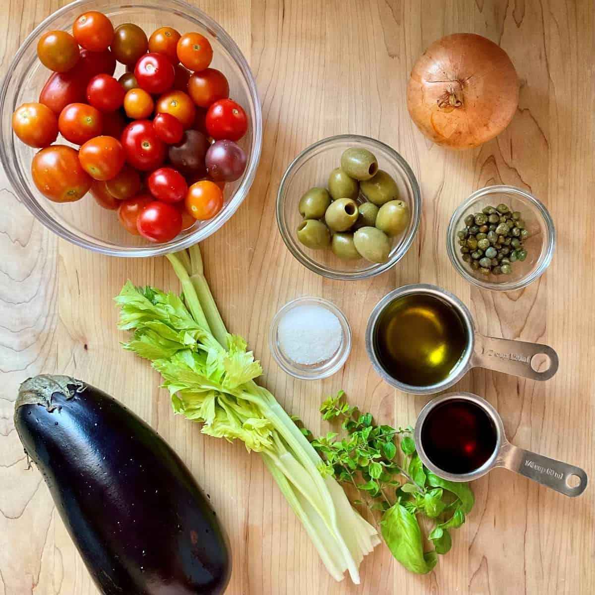 Ingredients for Sicilian-inspired eggplant caponata, including eggplant, cherry tomatoes, olives, capers, and fresh herbs.