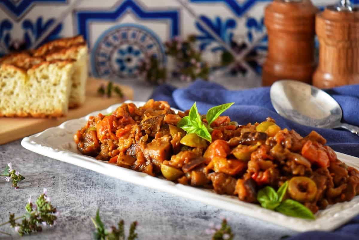 A white platter of caponata, a Sicilian-inspired dish with eggplant, tomatoes, olives, and capers.