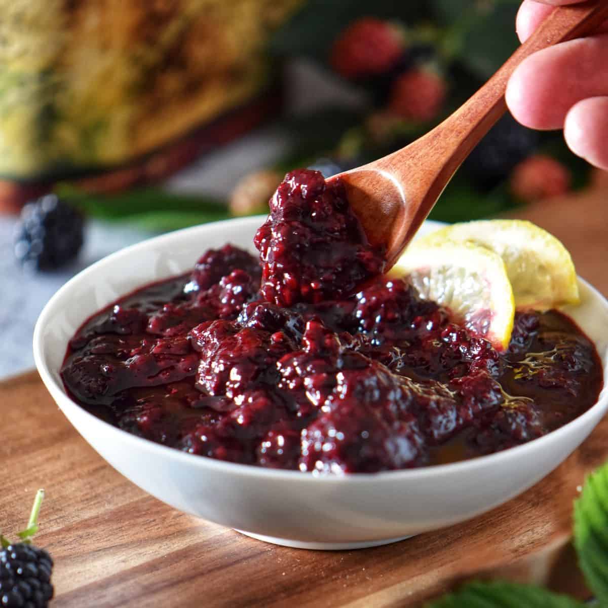 A spoonful of thick blackberry compote lifted from a bowl, highlighting the chunky fruit texture.