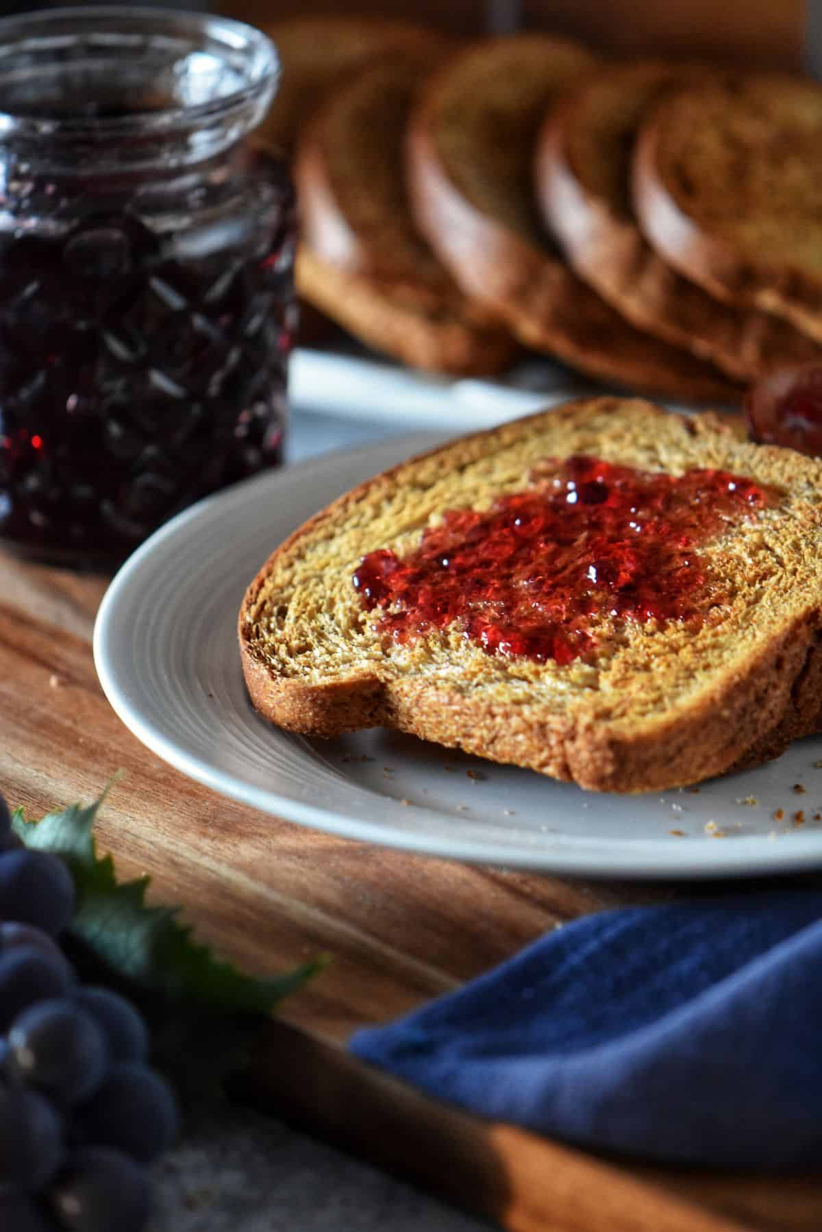 Homemade fette biscottate (Italian breakfast toast) served on a white plate with concord grape jelly.