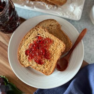 Italian fette biscottate on a plain white plate, spread with concord grape jelly.