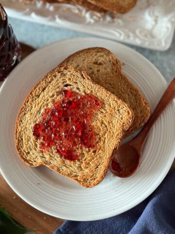Italian fette biscottate on a plain white plate, spread with concord grape jelly.