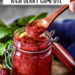 Wooden spoon holding raspberry compote with visible berry pieces.