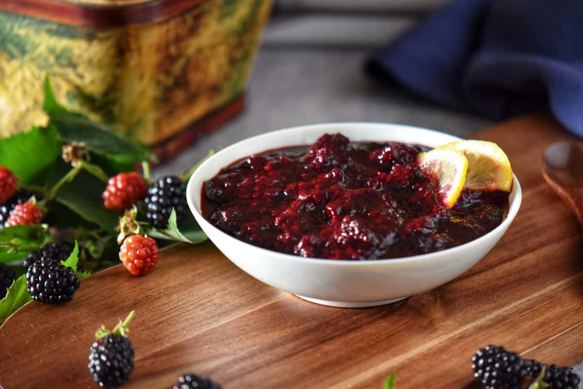 A bowl of homemade blackberry compote surrounded by fresh blackberries.