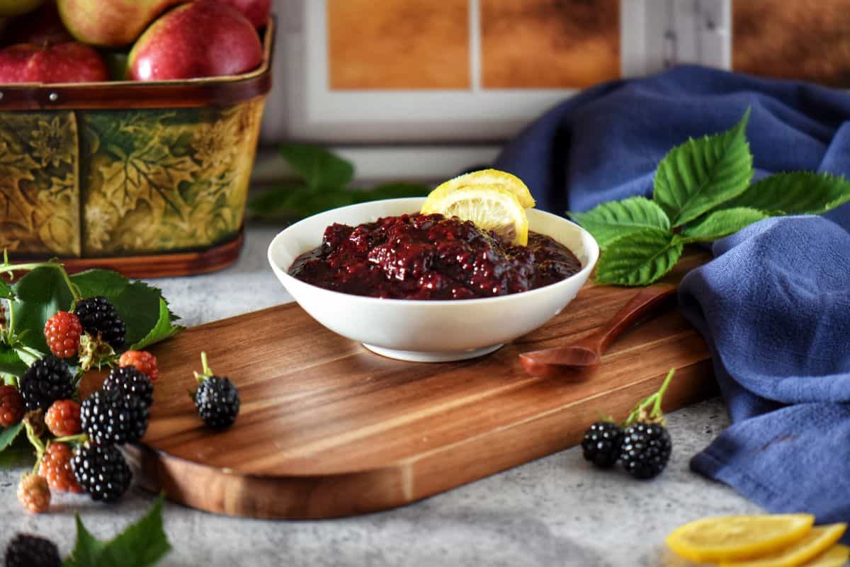 A bowl of homemade blackberry compote in a white bowl, surrounded by fresh blackberries.