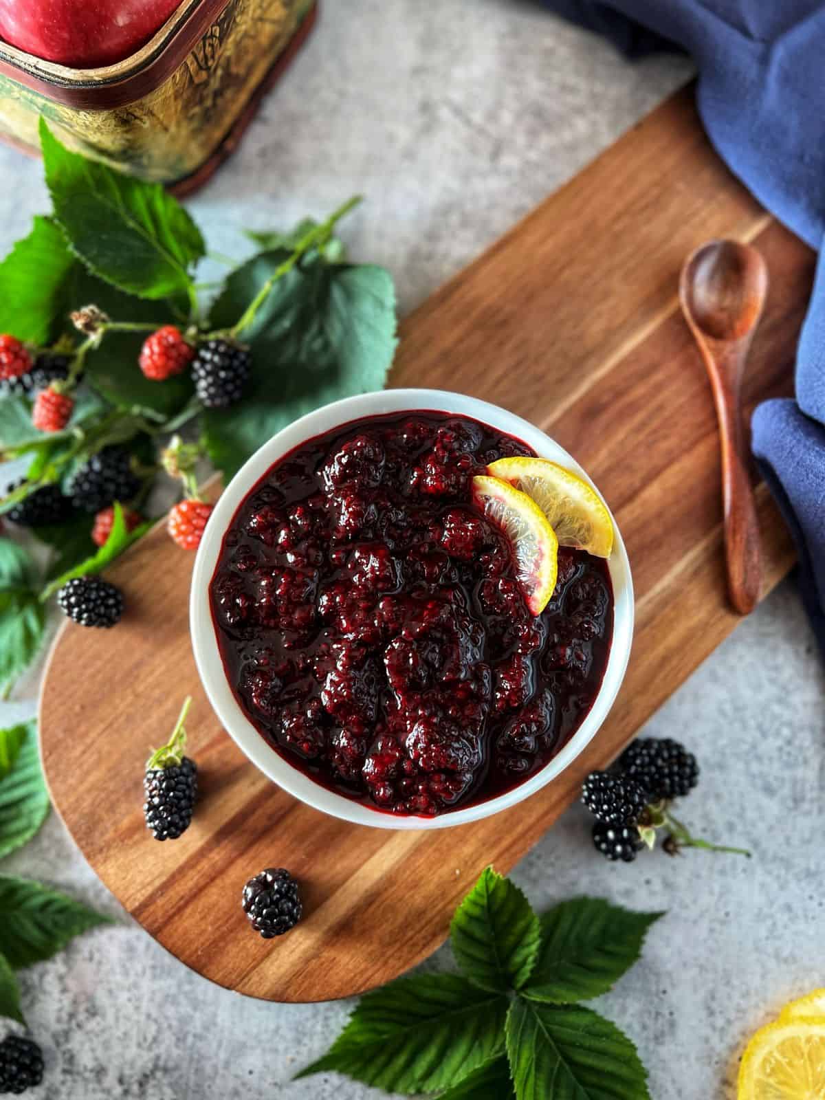 An overhead photo of a bowl of homemade blackberry compote surrounded by fresh blackberries.