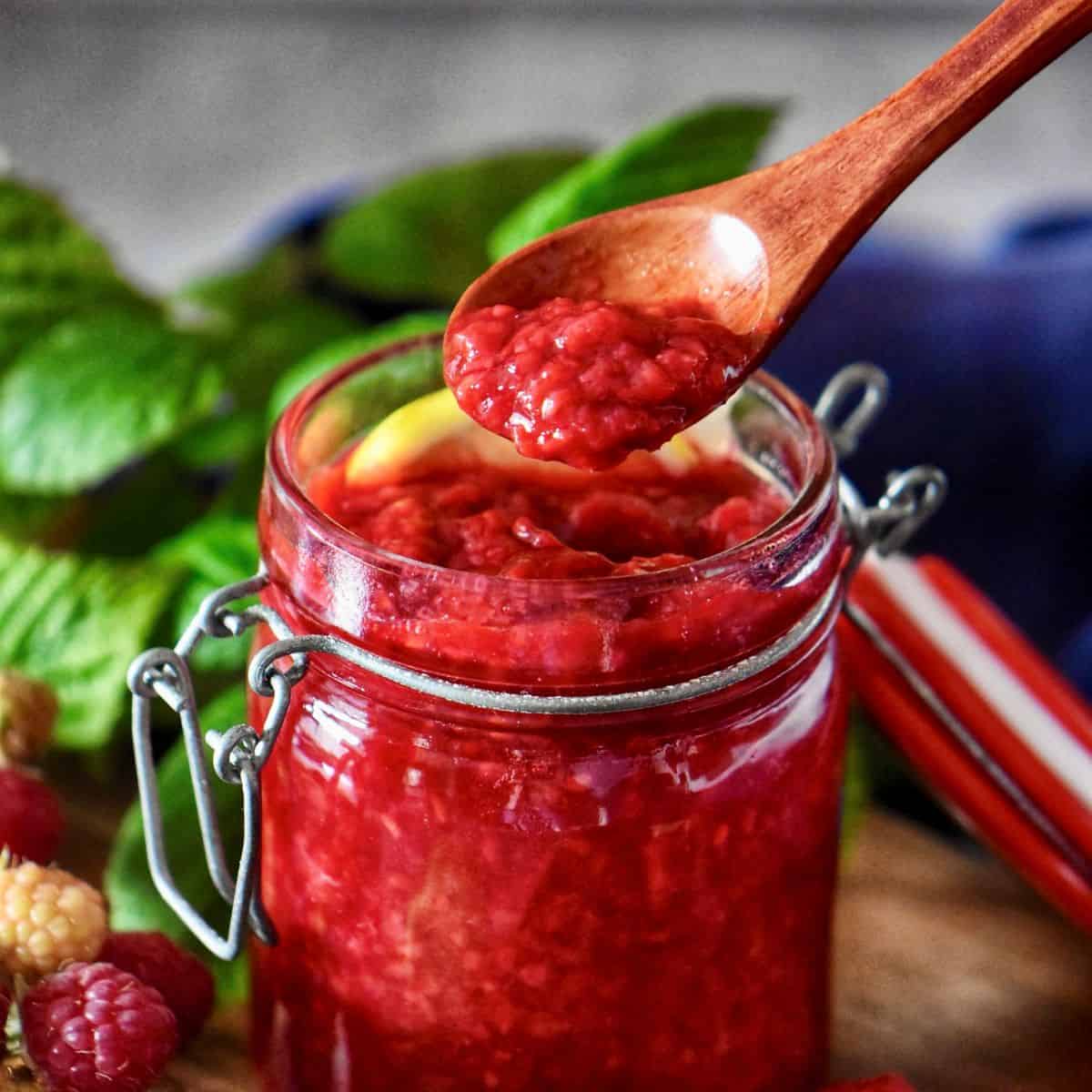 Wooden spoon holding ruby red raspberry compote with visible berry pieces.