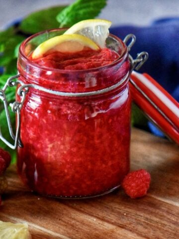 Raspberry compote in a mason jar with lemon garnish.