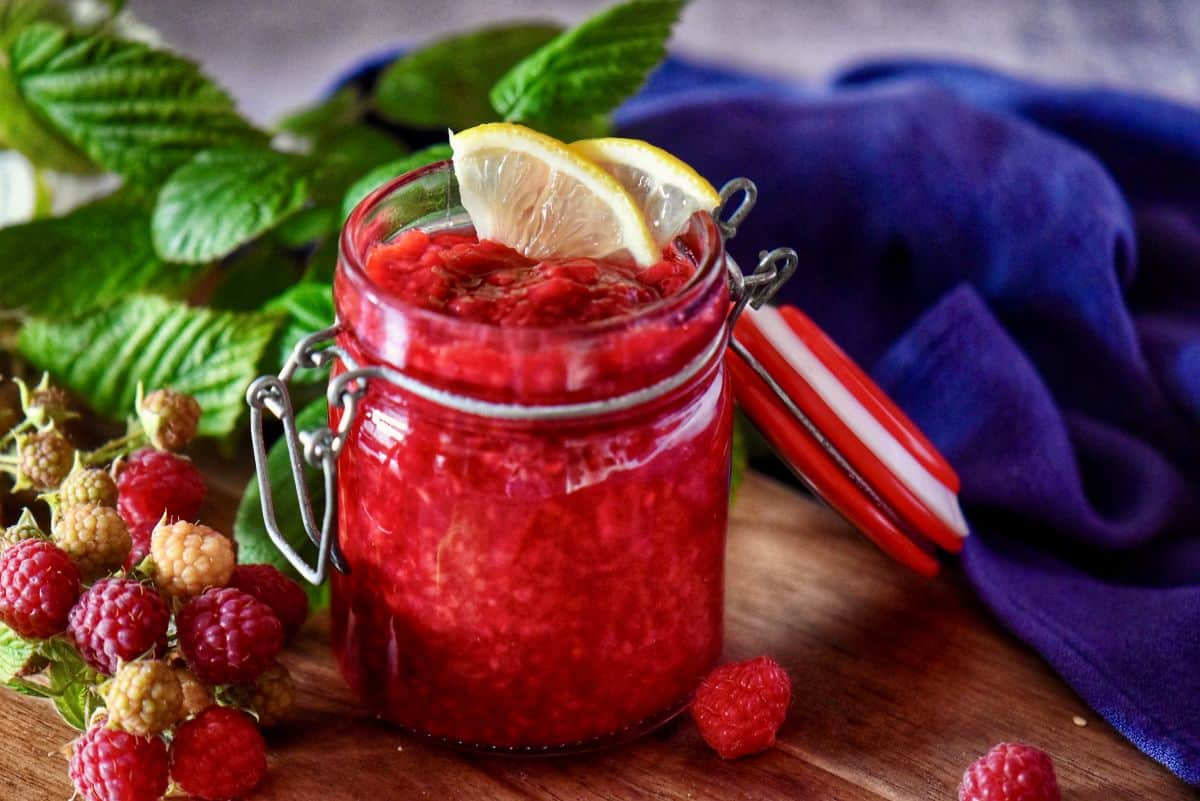 Mason jar of thick berry compote with fresh raspberries scattered around.