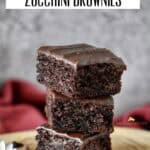 Squares of vegan zucchini brownies stacked on a wooden board, showing their fudgy texture.