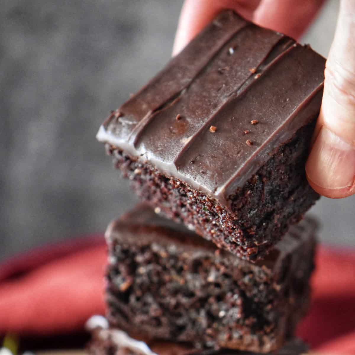 A hand holding a glazed zucchini brownie.