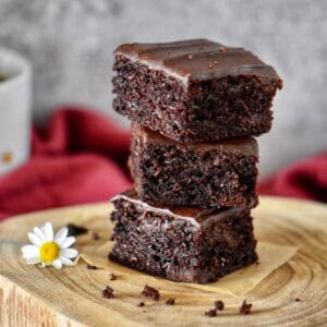 Squares of vegan chocolate zucchini brownies stacked on a wooden board, showing their fudgy texture.
