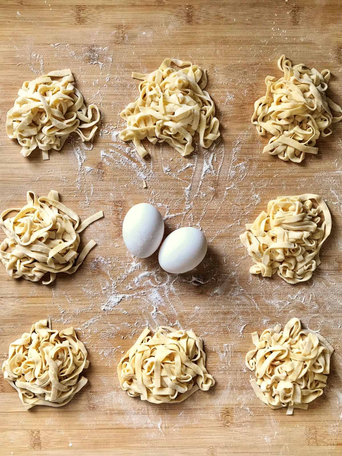 Thin ribbons of fettuccine made from traditional egg pasta dough on a wooden board next to two eggs.