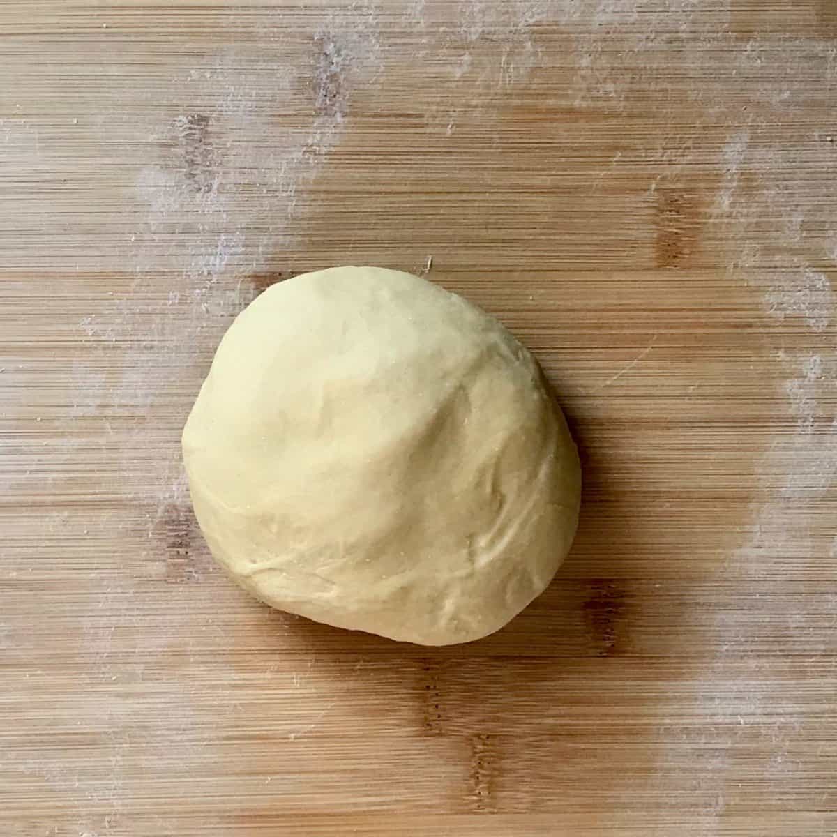 A ball of egg pasta dough on a wooden board.