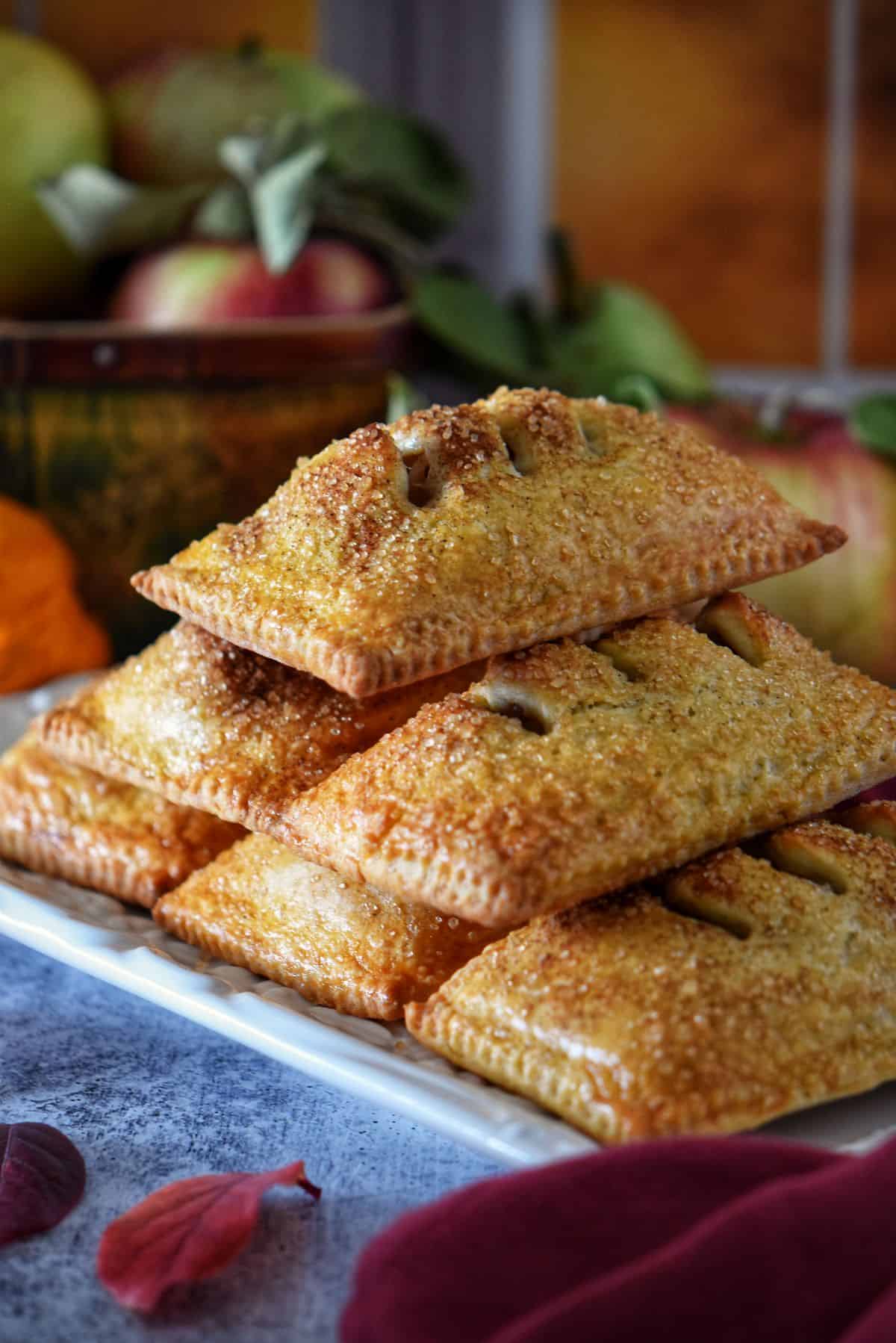 Golden brown apple hand pies with pasta frolla crust stacked on white plate, topped with cinnamon sugar.